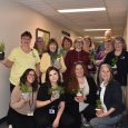 Thirteen employees gathered, holding plants they received.