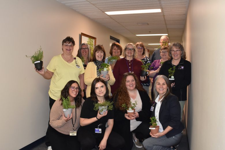 Thirteen employees gathered, holding plants they received.