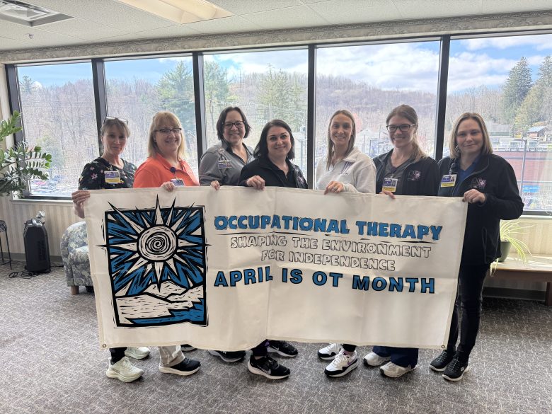 Seven ladies stand behind a banner celebrating Occupational Therapy month.