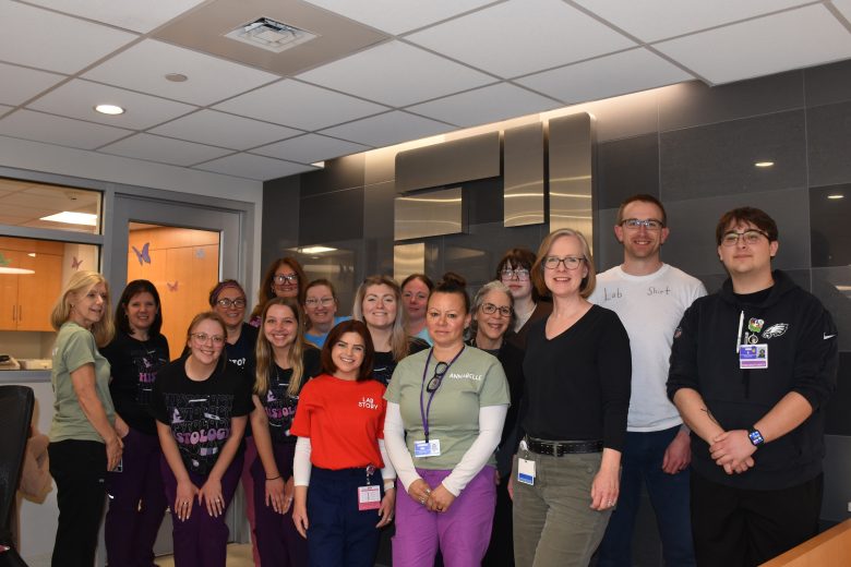 Sixteen employees together in front of hospital logo in main lobby.
