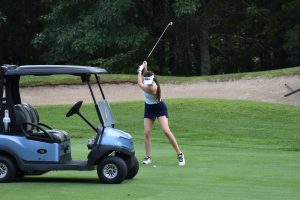 Women swinging a golf club next to a golf cart